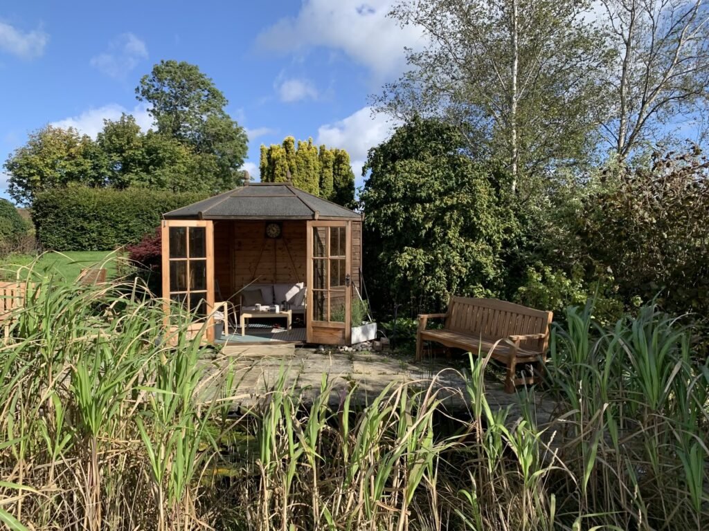 Open summerhouse and wooden bench beside the garden pond